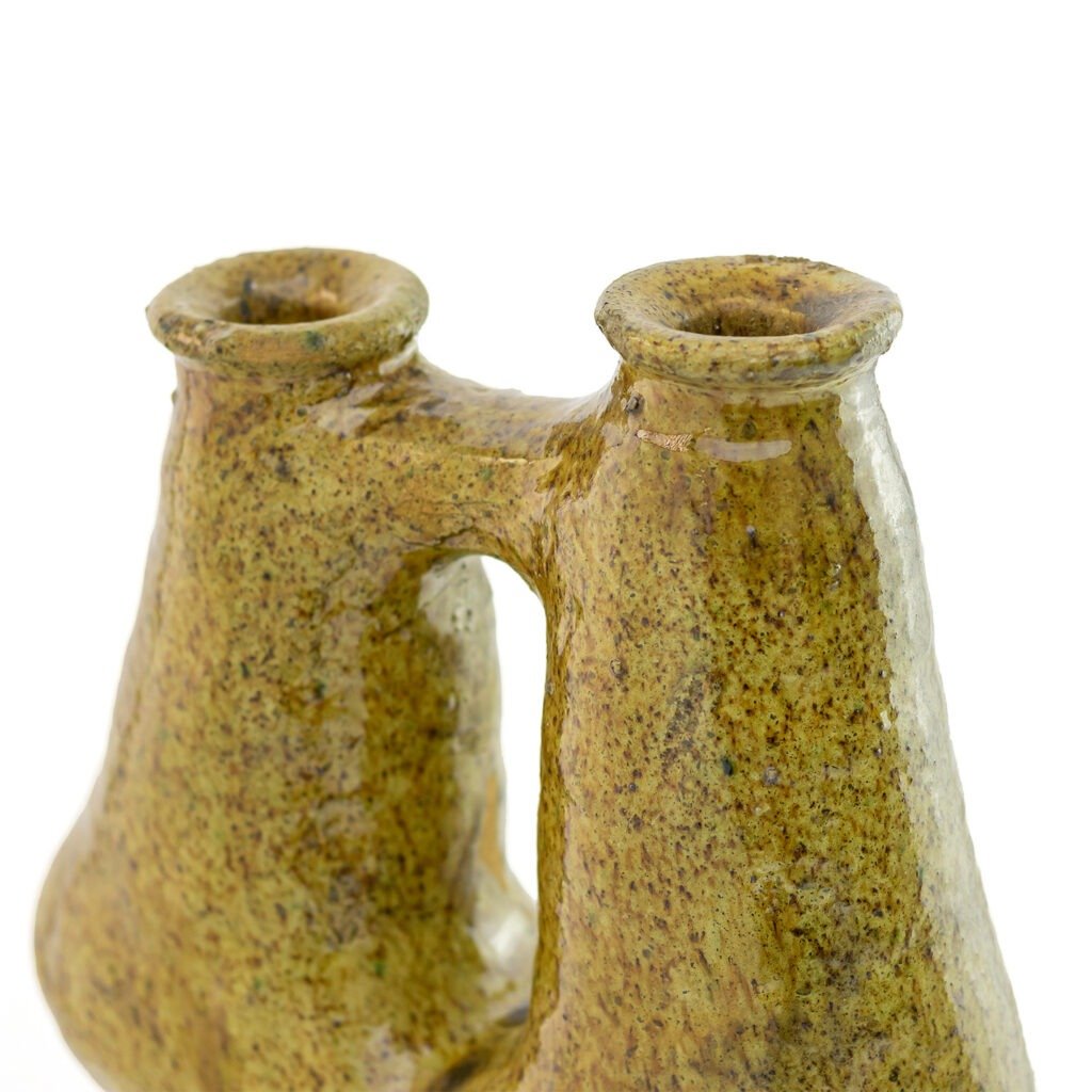 A ceramic double-neck vase inspired by Tamegroute pottery, with a textured, uneven glaze in earthy tones, featuring two openings and a connecting bridge.
