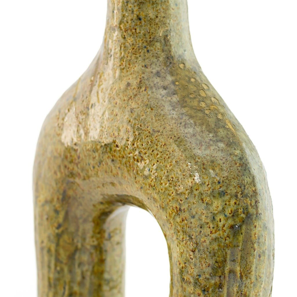 Close-up of a greenish sculptural ceramic with a glossy, textured surface, reminiscent of Tamegroute pottery, featuring an arching form and subtle speckled details.