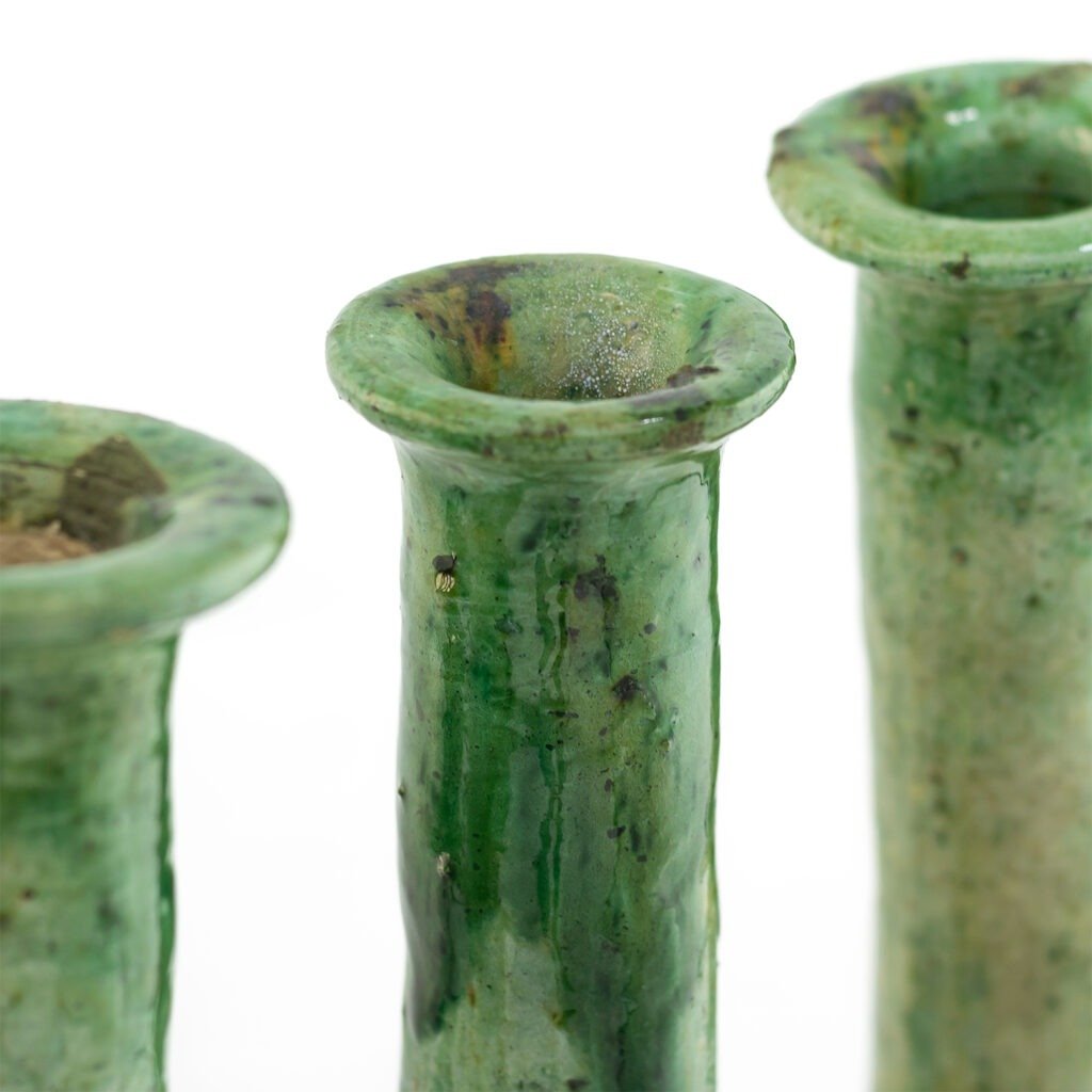 Close-up of three green ceramic vases with narrow openings and visible texture, resembling Tamegroute pottery, arranged in a row against a white background.