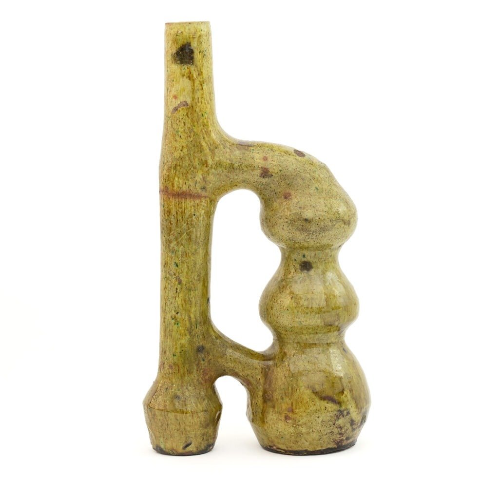 A greenish, abstract stone sculpture with an elongated shape, echoes the timeless artistry of Tamegroute pottery, featuring a tall, slender form and bulbous elements.