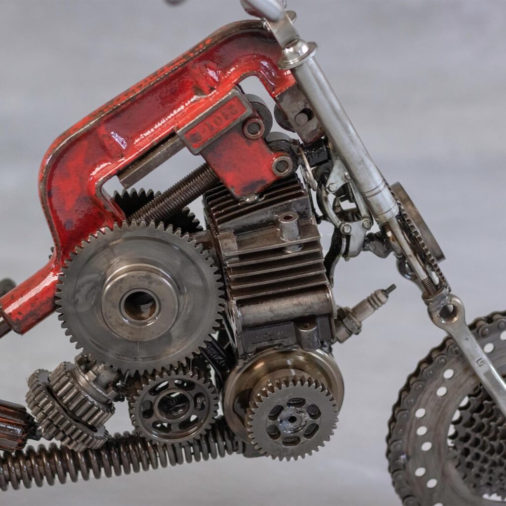 Close-up of a motorcycle metal art piece crafted from various mechanical parts, including gears, springs, and metal components, painted in rust-red and metallic colors. This captivating scrap metal sculpture showcases intricate craftsmanship.