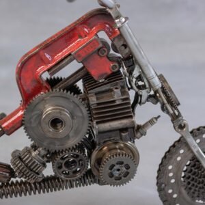 Close-up of a motorcycle metal art piece crafted from various mechanical parts, including gears, springs, and metal components, painted in rust-red and metallic colors. This captivating scrap metal sculpture showcases intricate craftsmanship.