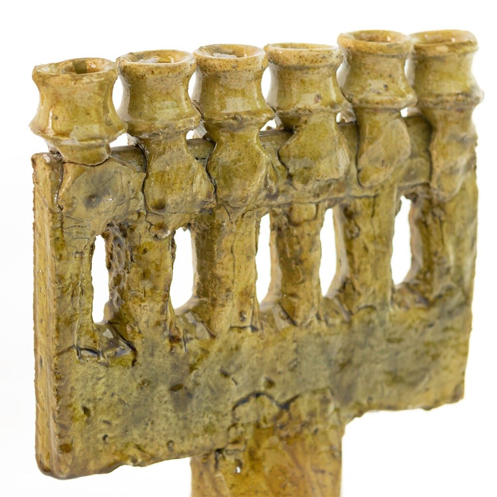 Close-up of a rustic, Tamegroute pottery menorah with six visible candle holders, featuring an earthy, textured surface.