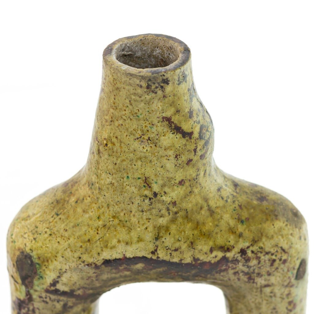 Close-up of a weathered, yellowish Tamegroute pottery piece with a hollow, cylindrical top and a roughly textured surface, showing discoloration and signs of aging.