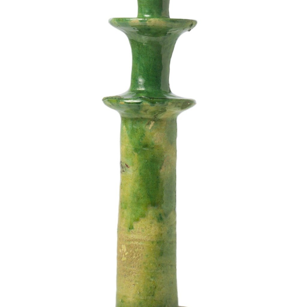 A green ceramic candle holder, inspired by Tamegroute pottery, boasts a glossy finish and features a tall, slender design with two rounded platforms.