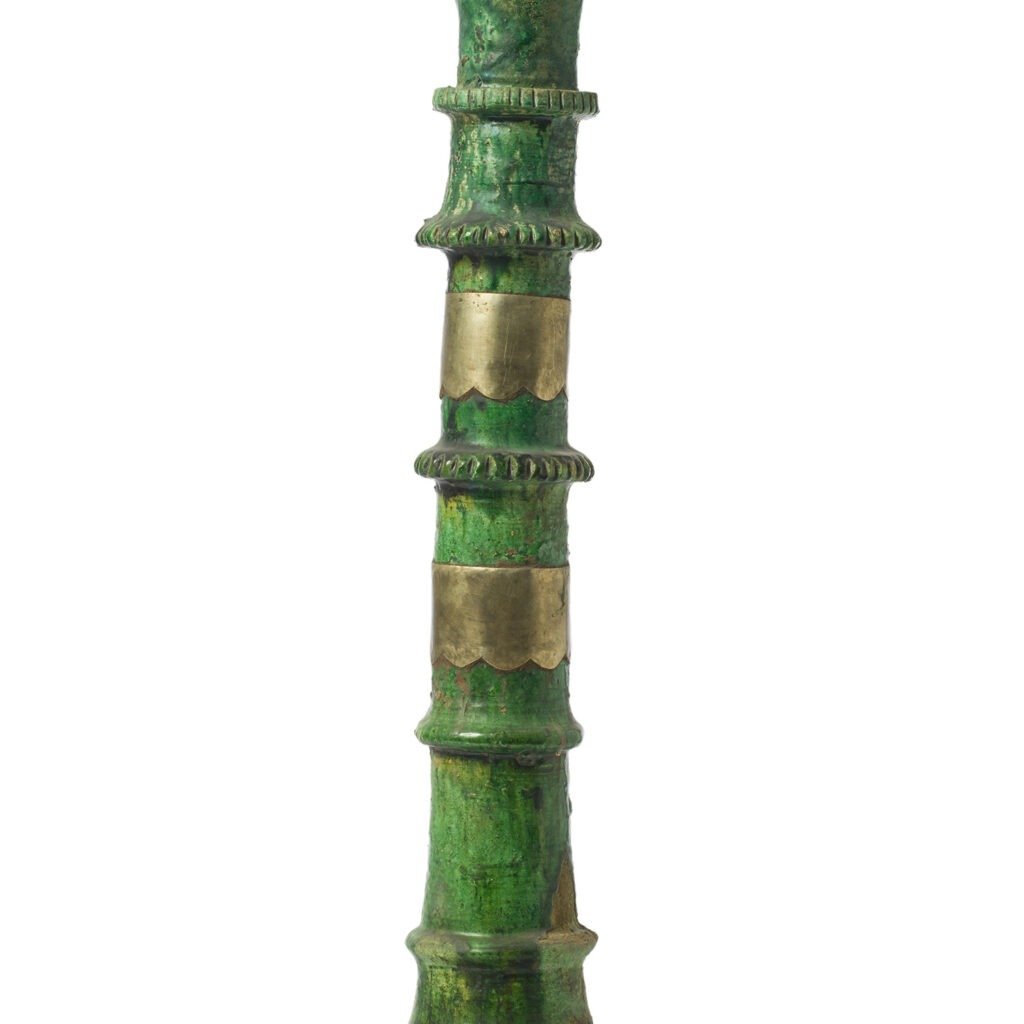 A vertical, green, bamboo-like column with brass bands evokes the timeless elegance of Tamegroute pottery.