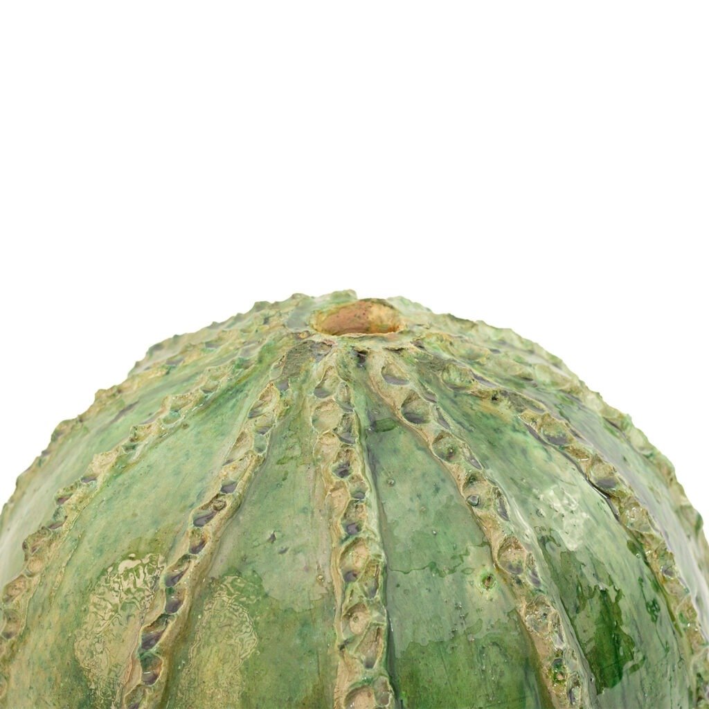 Close-up of the top of a green, textured melon reminiscent of Tamegroute pottery against a plain white background.