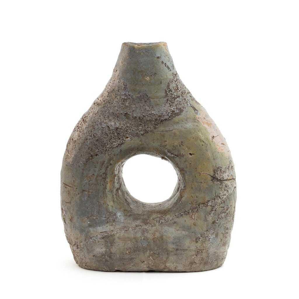 A rustic, weathered stone vase reminiscent of glazed Tamegroute pottery, with a triangular shape and a circular hole in the center, stands upright against a white background.