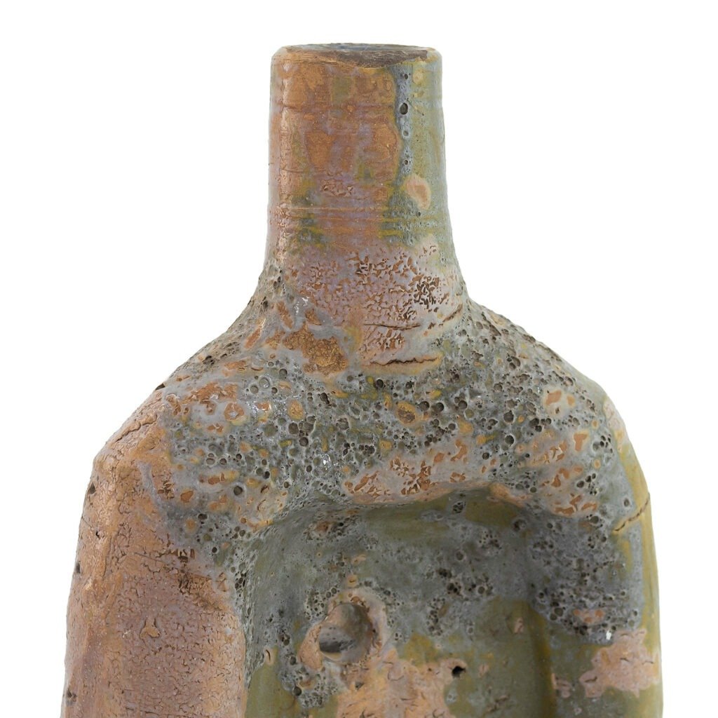 Close-up view of a textured ceramic vase with earth-toned glazes in shades of green and brown, reminiscent of Tamegroute pottery, featuring a cylindrical neck and an irregular surface.