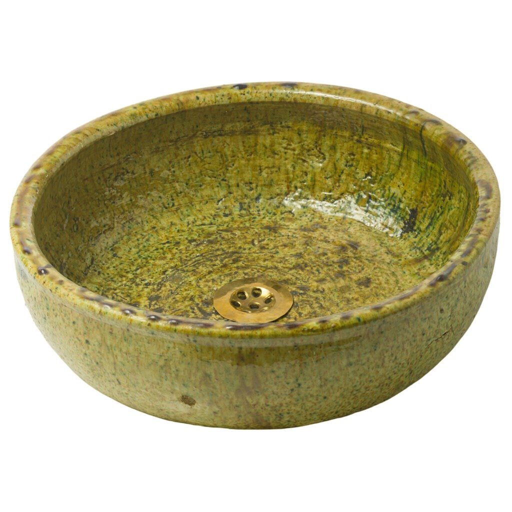 This round, green ceramic sink, crafted in the style of Tamegroute pottery, features a textured surface and a brass drain at the bottom.