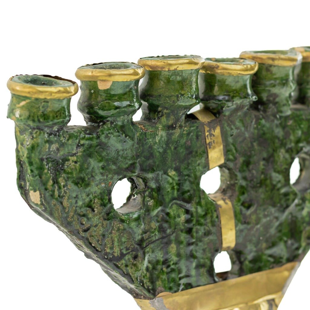 Close-up of a green Tamegroute pottery menorah with a textured surface, featuring seven candle holders and gold accents.