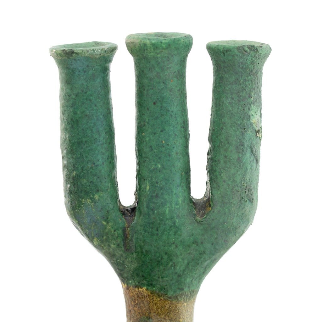 A green, ancient-looking metal trident, reminiscent of Tamegroute pottery with its earthy hues and weathered texture, stands upright with its three prongs and a worn surface.