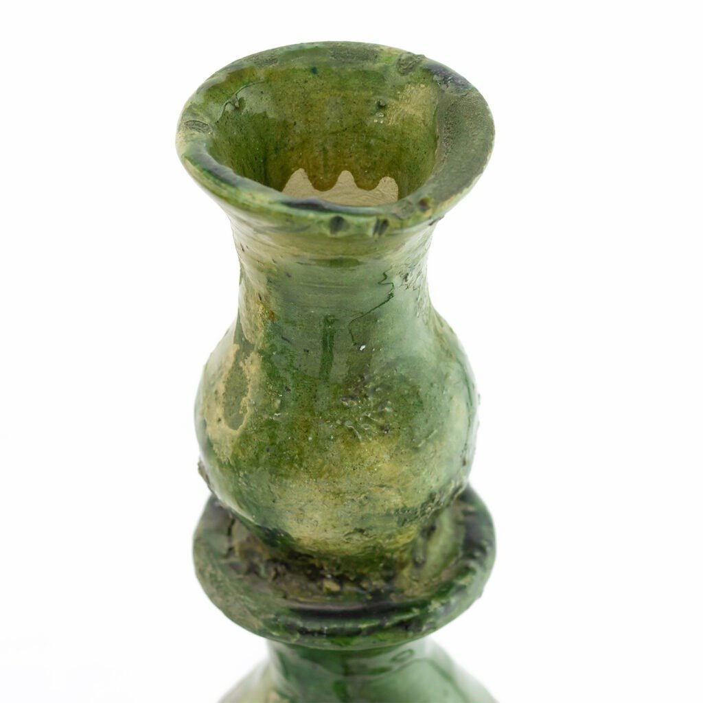 A close-up of an aged, ceramic green vase with a narrow, wavy-edged opening and bulbous midsection, reminiscent of traditional Tamegroute pottery craftsmanship.