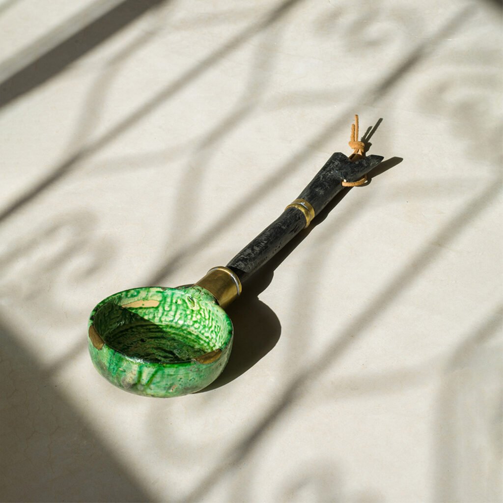A green ceramic ladle with a black and brass handle sits gracefully on a sunlit surface, casting intricate shadows.