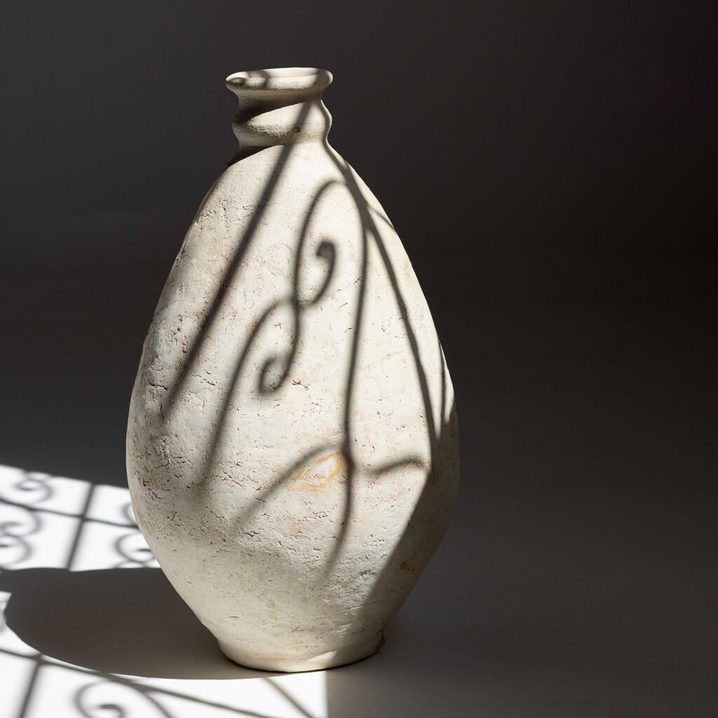 A tall, textured ceramic vase basks in soft light, casting delicate shadows. Its surface dances with intricate patterns, reflecting artistry reminiscent of a skilled potters hand.
