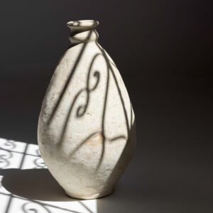 A tall, textured ceramic vase basks in soft light, casting delicate shadows. Its surface dances with intricate patterns, reflecting artistry reminiscent of a skilled potters hand.