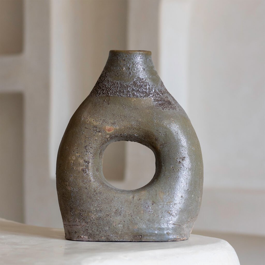 A piece of tamegroute pottery, this ceramic vase features a textured, grayish surface and a hollow center, elegantly resting on a light, smooth surface.