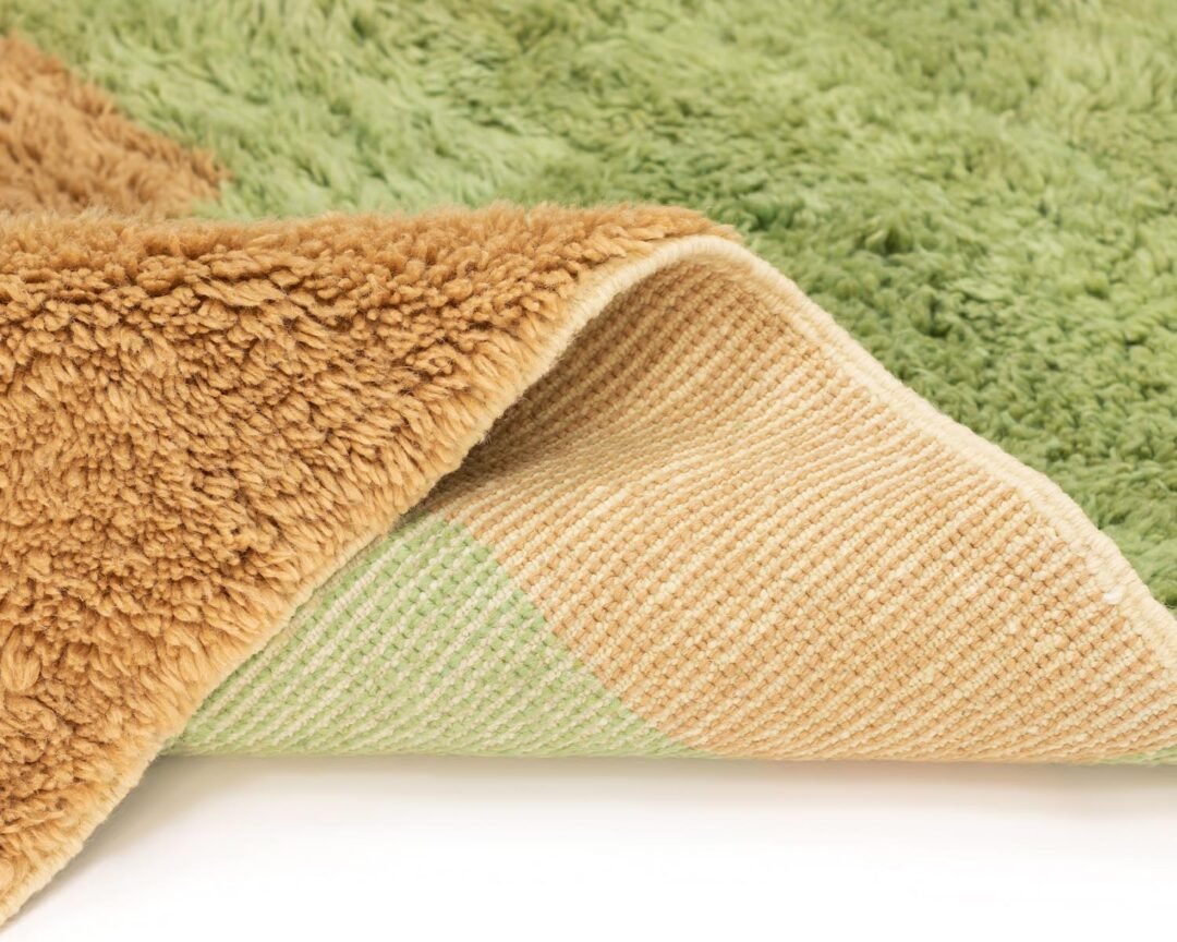 Close-up of a luxurious brown and green plush rug with a folded corner revealing a striped underside, showcasing its hand-knotted texture and color contrast.