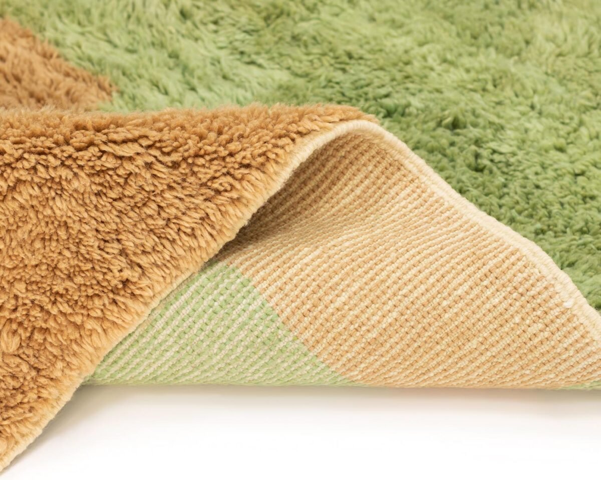 Close-up of a luxurious brown and green plush rug with a folded corner revealing a striped underside, showcasing its hand-knotted texture and color contrast.