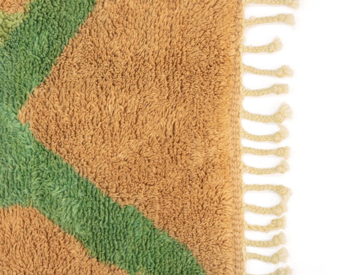 Close-up of a luxurious, hand-knotted rug corner with intricate brown and green patterns, featuring beige fringes on the edge.