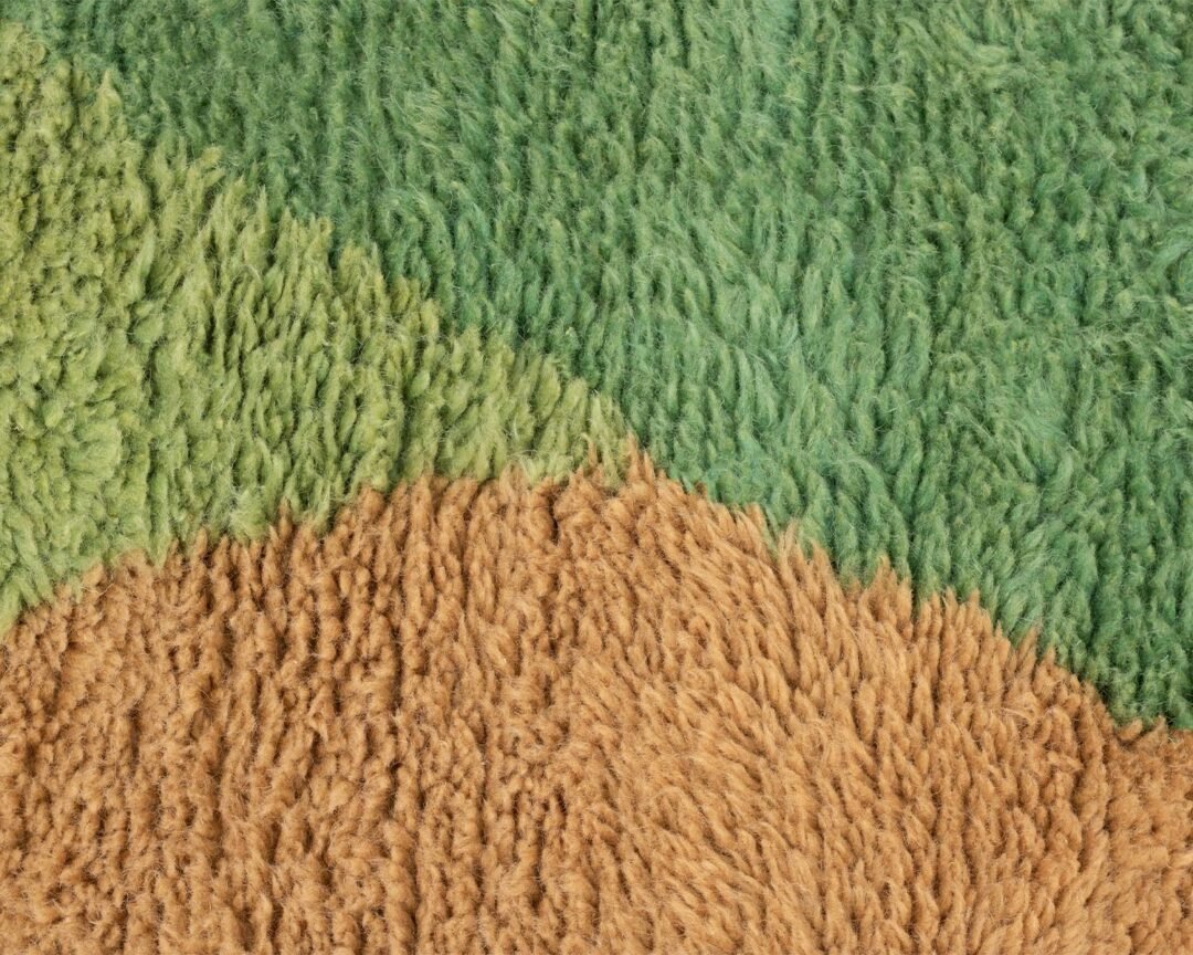 A close-up of a textured, multicolored carpet with overlapping green and beige sections, resembling a grassy landscape—perfect for those seeking luxury rugs to elevate their home decor.