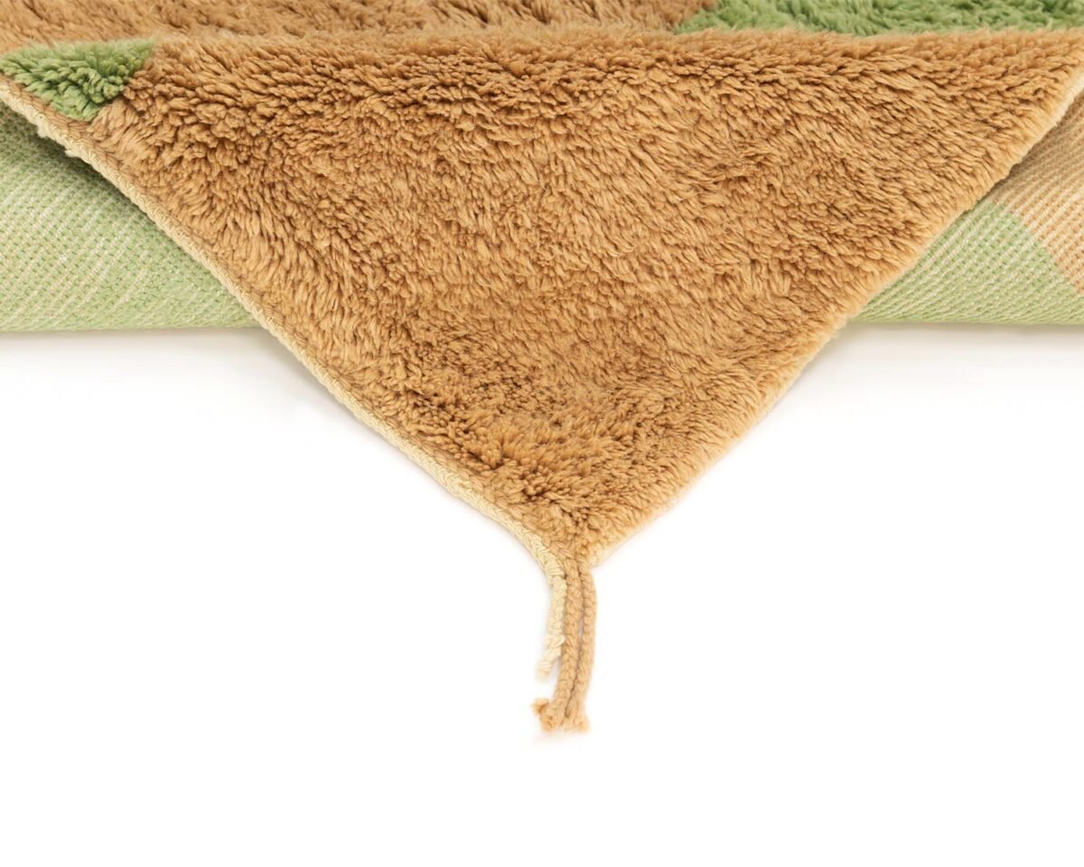Experience the elegance of luxury rugs with this corner view of a folded, textured masterpiece. Featuring a brown and green checkered design and exquisite tassel details, this handmade home decor piece brings sophistication to any space.