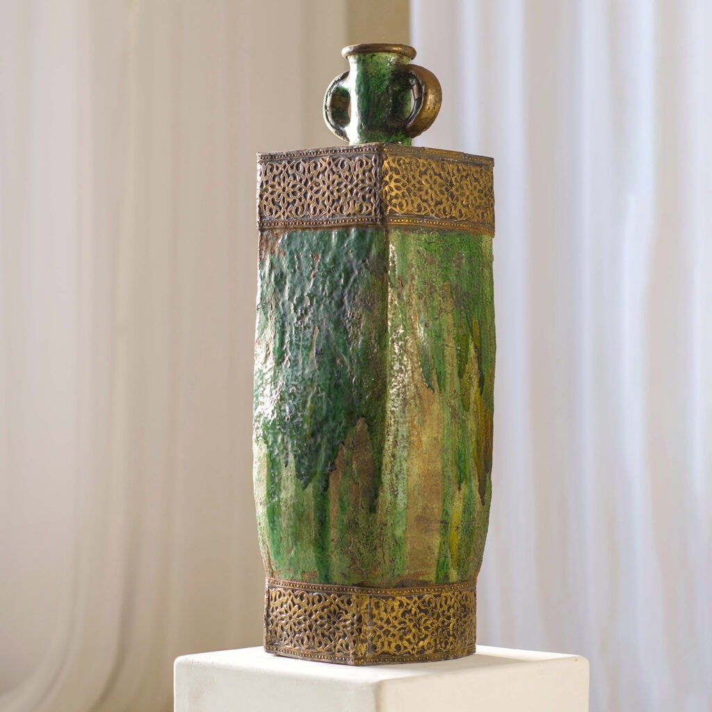 This elegant, tall green ceramic vase features a square base, ornate gold trim, and two small handles. It adds a touch of sophistication and stands proudly on its pedestal.