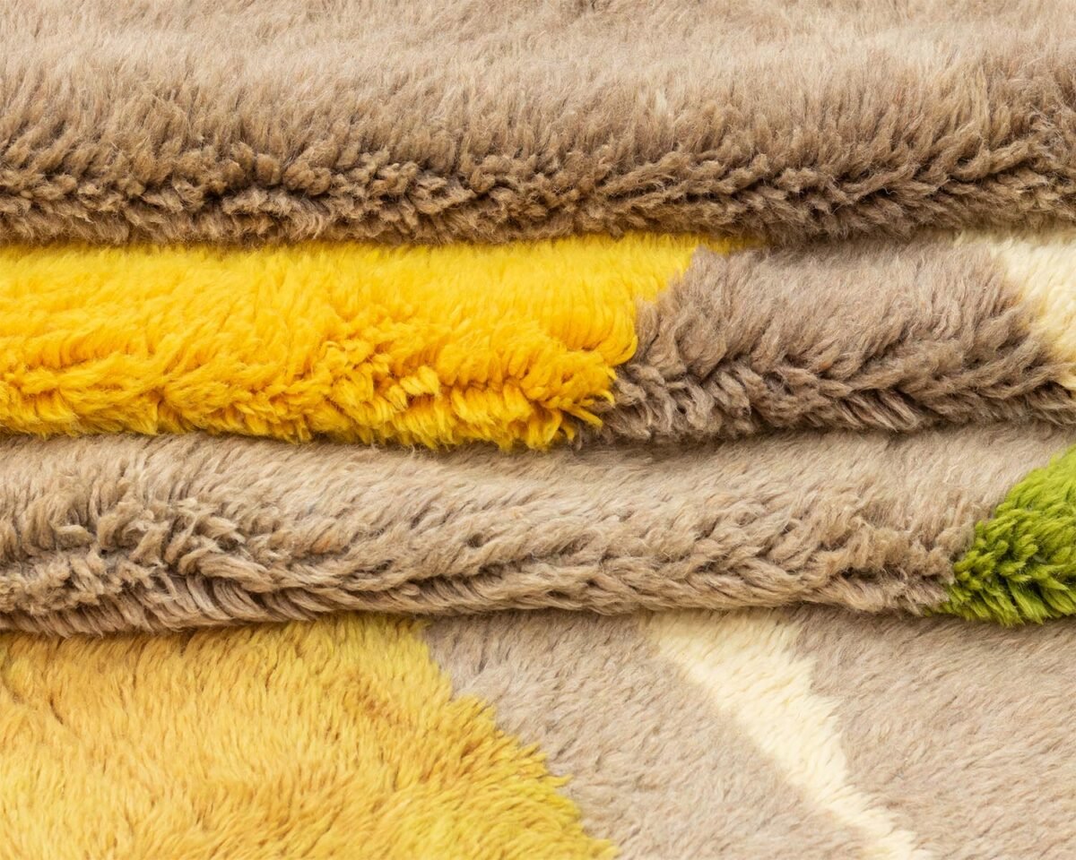 A close-up captures the intricate texture of these soft, hand-knotted rugs, featuring sections of beige, yellow, and green in a stunning play of colors.
