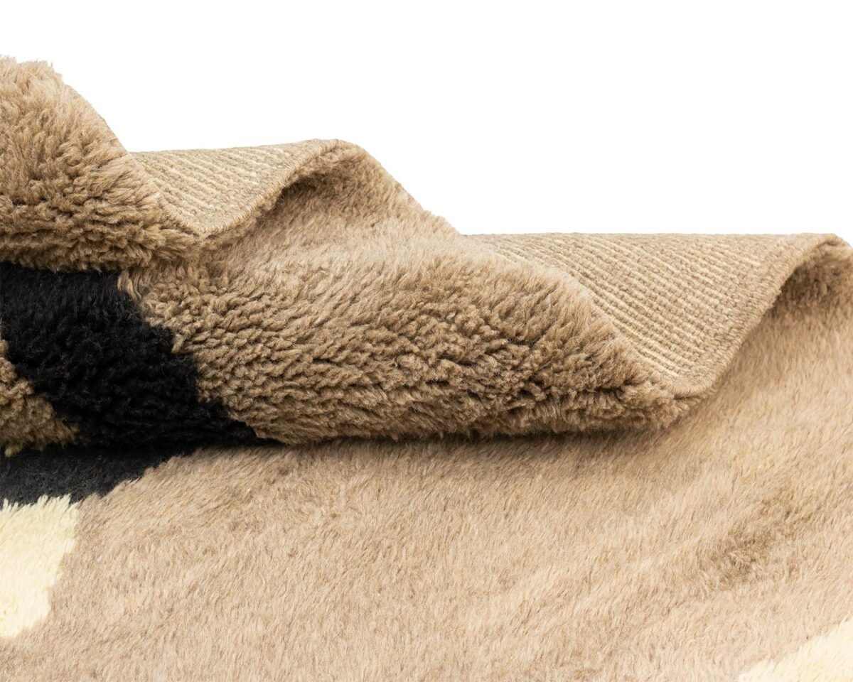 A close-up of a textured, hand-knotted surface in beige and black, reminiscent of a Moroccan rug.