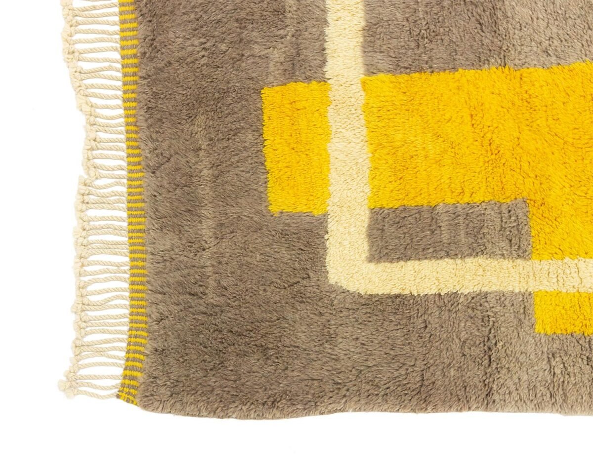 Close-up of a hand-knotted Moroccan rug with fringe, featuring a geometric pattern in yellow, gray, and cream.