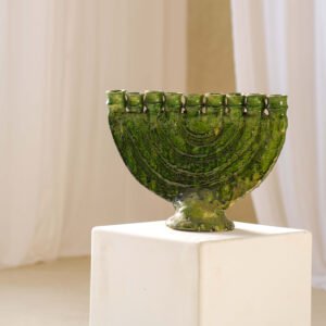 A stunning green ceramic menorah with nine candle holders elegantly displayed on a white pedestal, set against a warm beige background.