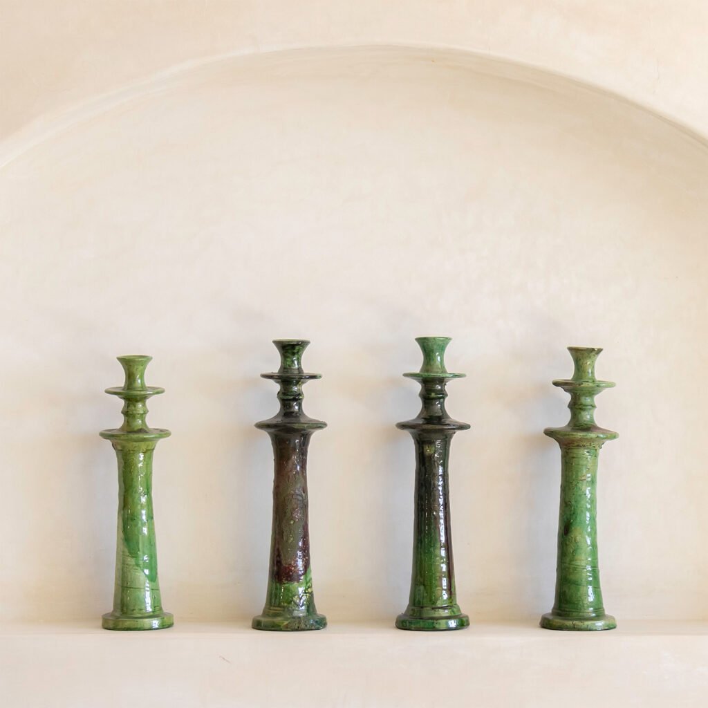 Four green ceramic vases of varying shades are arranged elegantly in a row against a light, textured wall. Each vase adds a touch of natural beauty and sophistication to the decor, creating an inviting and serene atmosphere.
