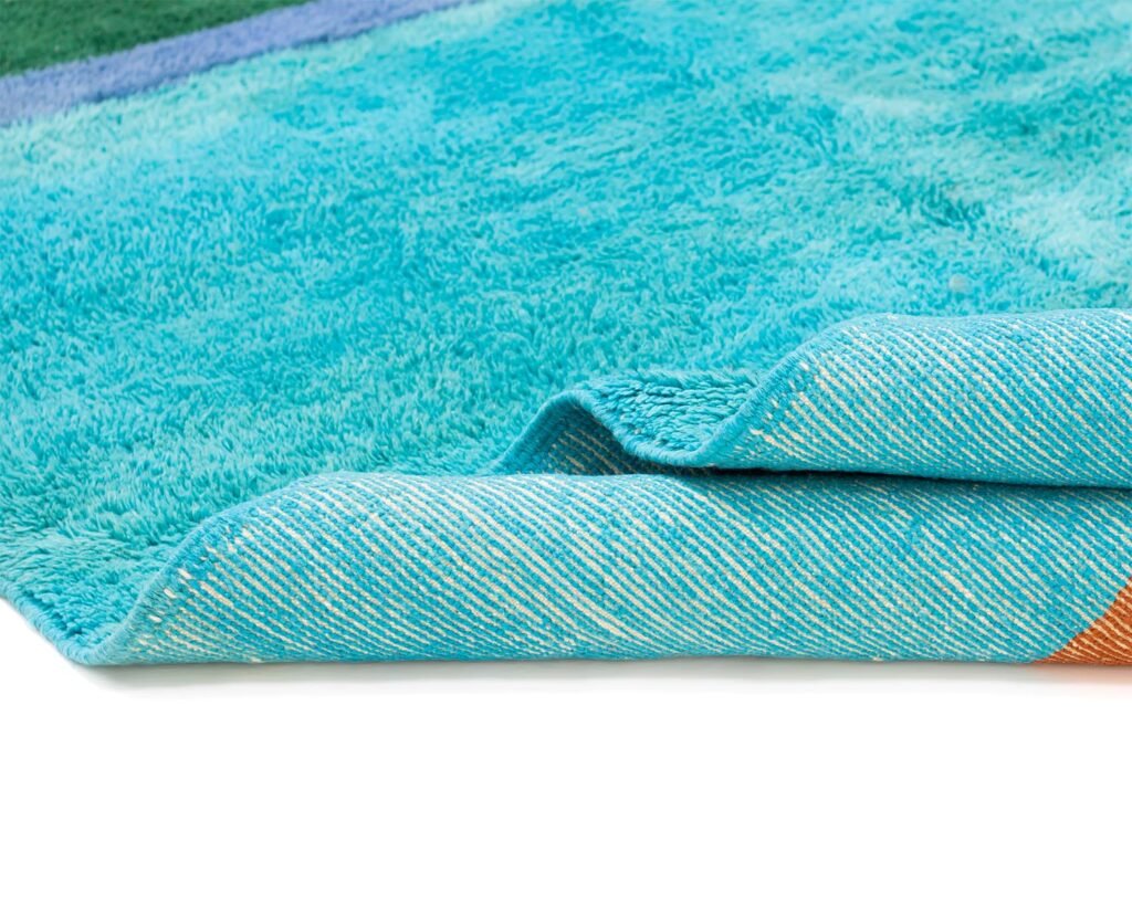 Close-up of a hand-knotted luxury rug in aqua blue with visible texture and intricate stitching, elegantly placed on a pristine white surface.