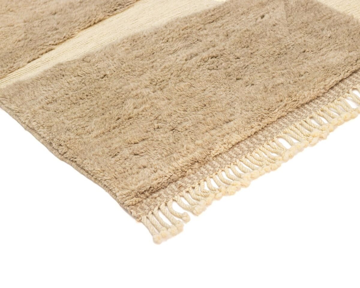 Experience the elegance of a luxury rug with this close-up of a beige textured piece, showcasing intricate hand-knotted craftsmanship and fringe details. Its thick, soft material exudes warmth and sophistication, adding a touch of handmade home decor to any space.