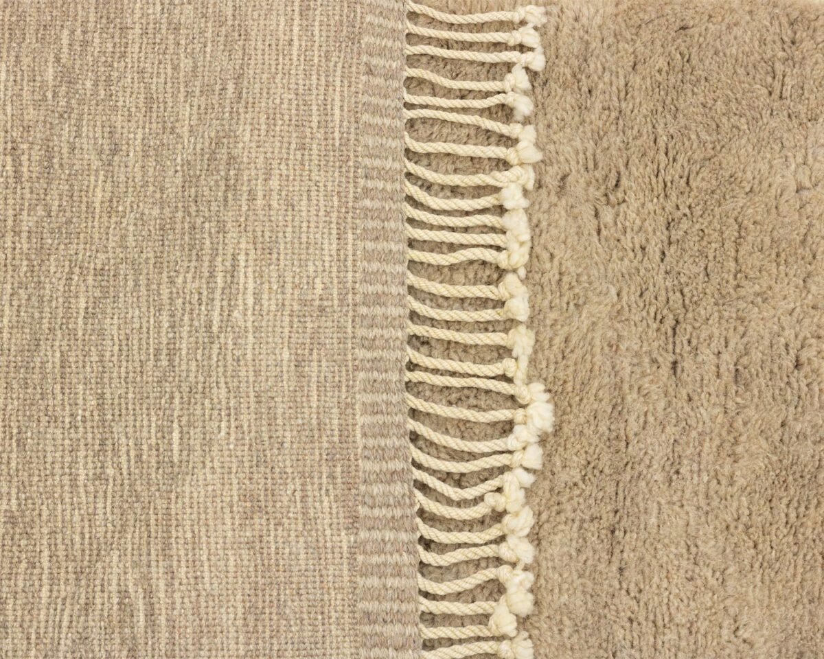 This exquisite close-up showcases a luxury rug featuring beige textured fabric with a fringe border. The left side is tightly woven, while the right flaunts a fluffy texture, with twisted tassels adding an artisanal touch to this handmade home decor piece.
