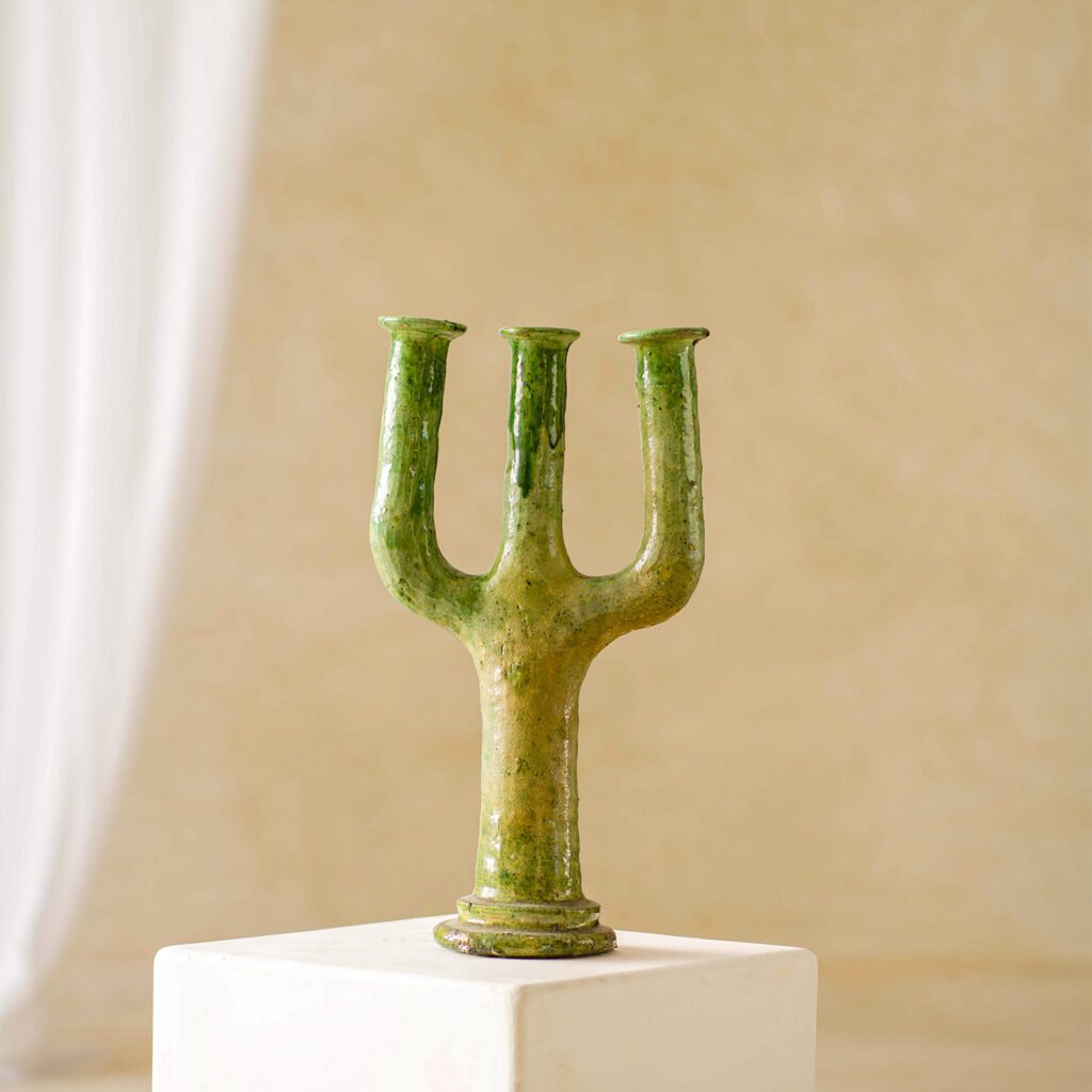 A vibrant green, three-pronged ceramic sculpture elegantly rests on a white pedestal against a subtle, neutral backdrop.