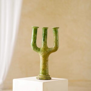 A vibrant green, three-pronged ceramic sculpture elegantly rests on a white pedestal against a subtle, neutral backdrop.