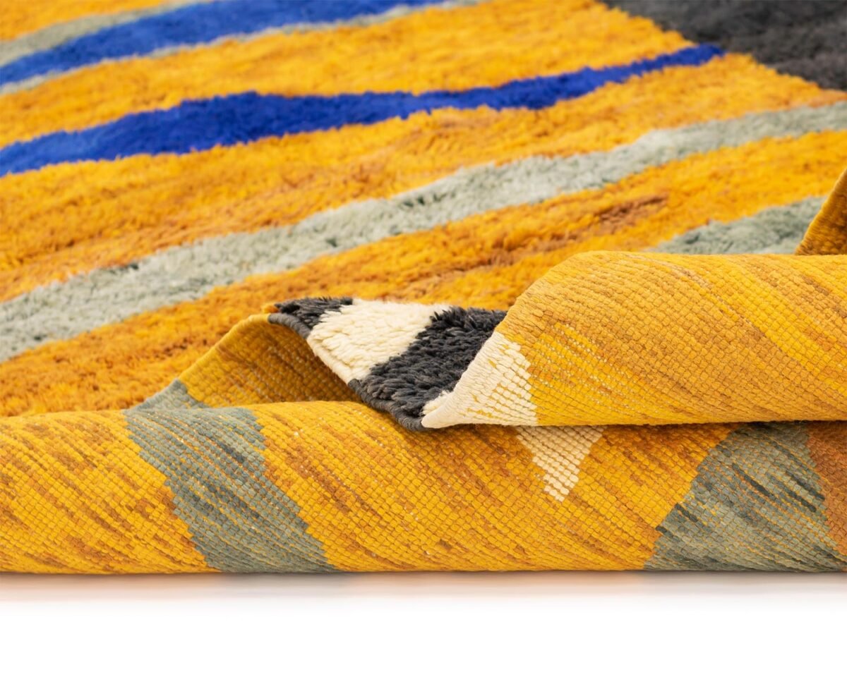 Heres a detailed look at a luxurious hand-knotted rug, boasting vibrant orange, yellow, blue, and gray geometric patterns. The corner is elegantly folded over, showcasing its intricate design.