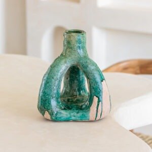 A green and beige ceramic vase with an open, sculptural design sits elegantly on a light-colored table, adding a touch of artistry to the space.