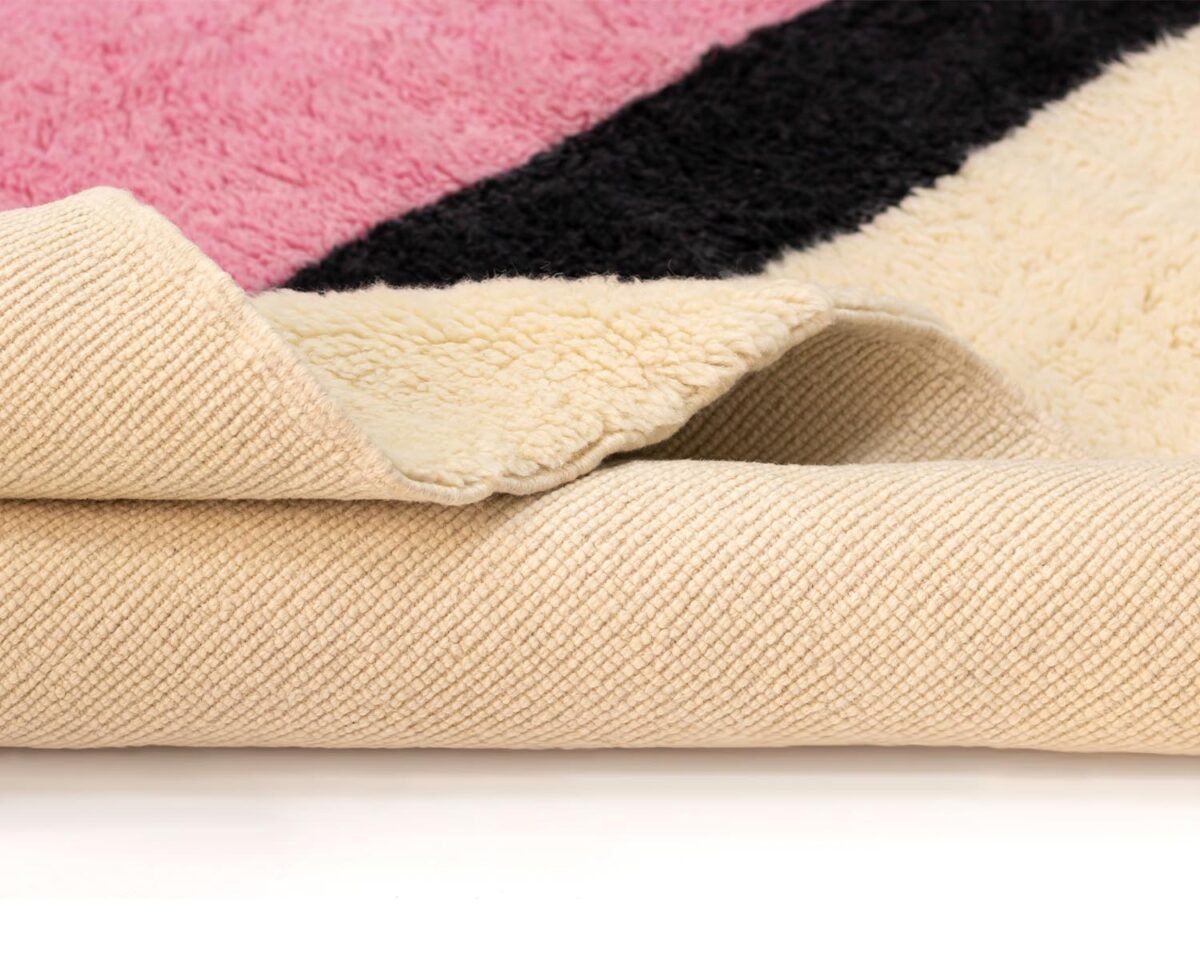 Close-up of a folded rug highlighting a pink, black, and beige pattern with a detailed textured underside in light beige.