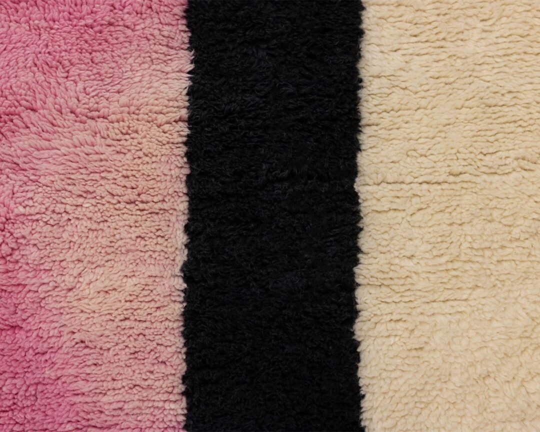 A close-up of a textured surface featuring three vertical stripes: pink, black, and cream, from left to right. The intricate pattern adds an artistic flair to the design.