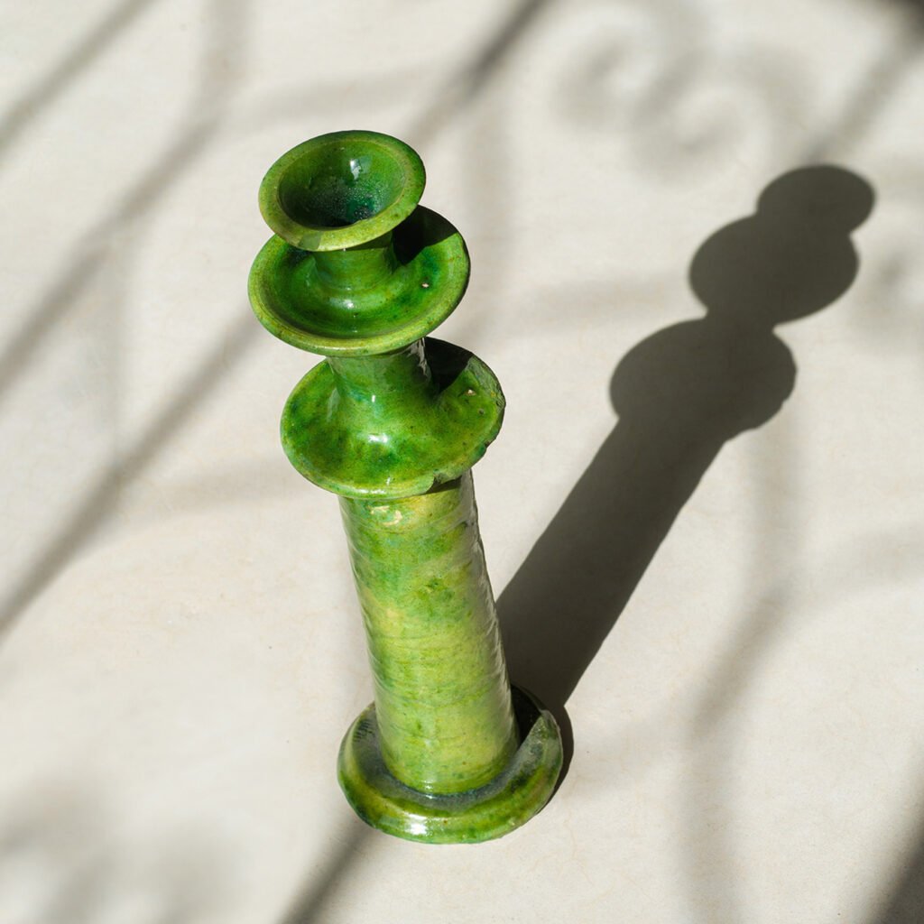 A green ceramic candlestick holder casting an elegant shadow on a light surface brings a touch of sophistication to any space.