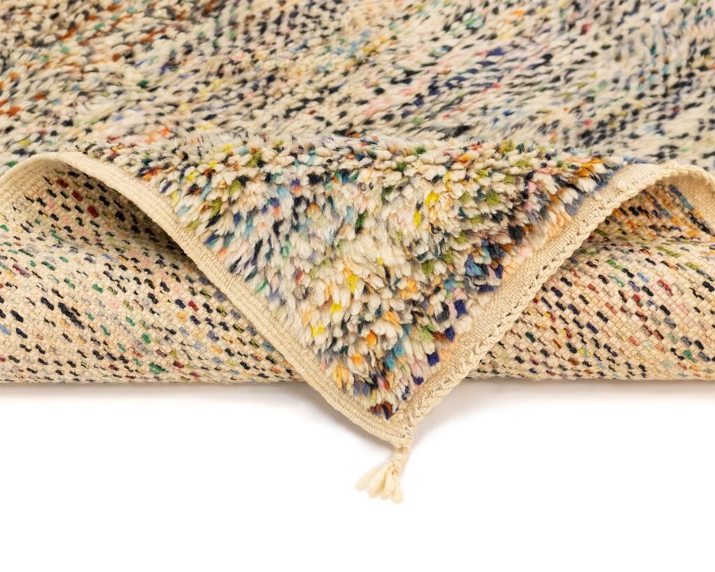 This luxurious close-up showcases a multicolored, hand knotted rug with a fluffy pile and woven underside. The corner is folded to reveal the intricate handmade design, featuring vibrant colors on a neutral background.