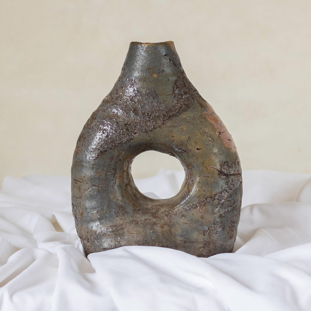 A textured Tamegroute pottery vase with an earthy glaze, featuring a central hole, stands on a white cloth background.