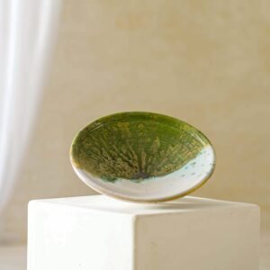 A small, speckled green ceramic bowl rests elegantly on a white pedestal, set against a neutral background.