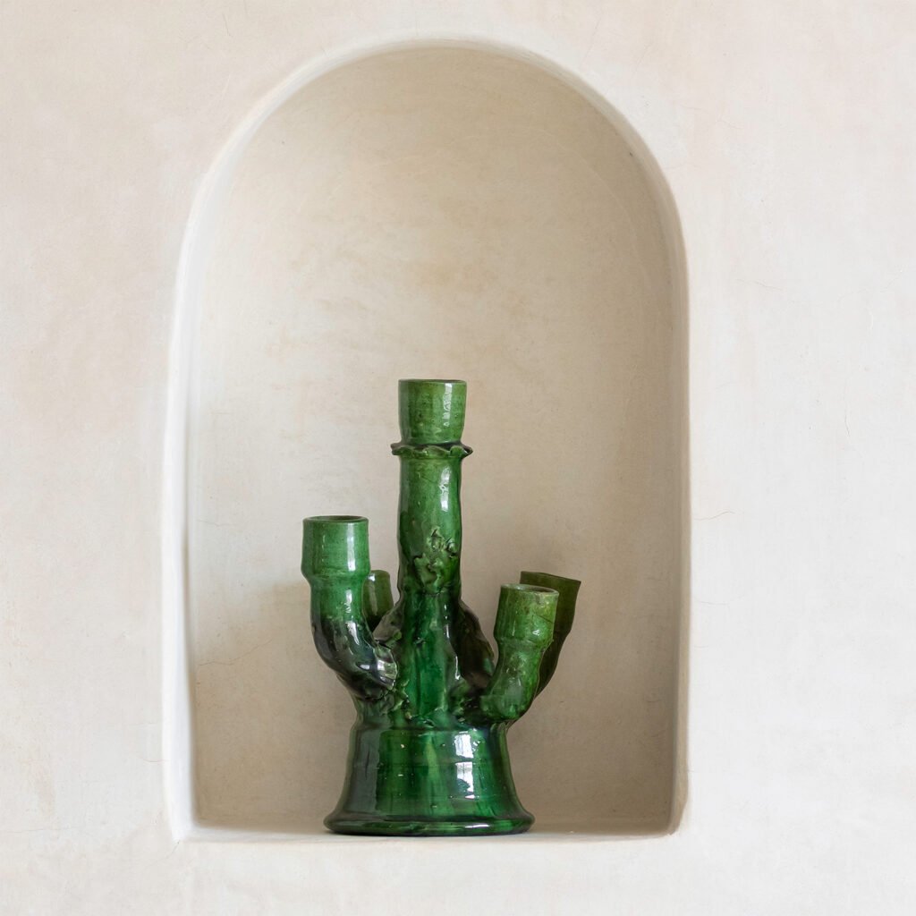 A green ceramic vase with three upward branches elegantly graces a white recessed wall niche, adding a touch of nature-inspired charm.