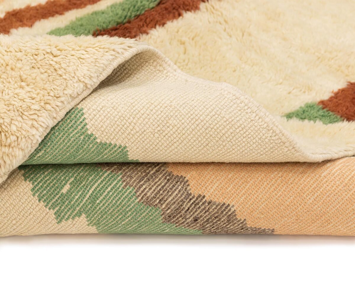 This close-up features a luxury rug showcasing both sides: one adorned with a colorful abstract pattern in green, orange, and brown, and the other offering an off-white fluffy texture.