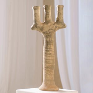 An ancient pottery artifact with three prongs stands upright on a pedestal, set against a light backdrop.