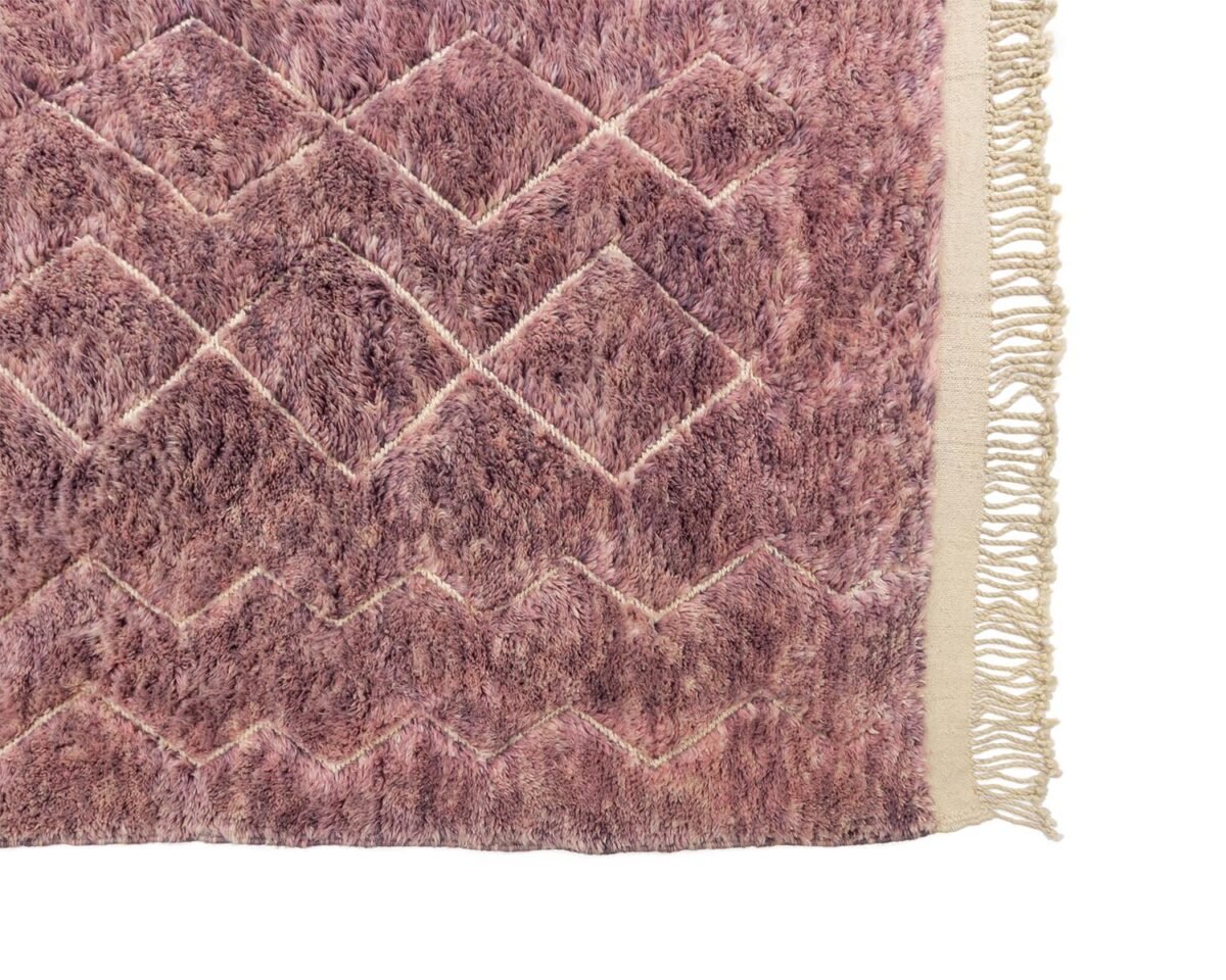 Close-up of a hand knotted, textured purple shaggy rug with diamond patterns and fringe along the right edge.