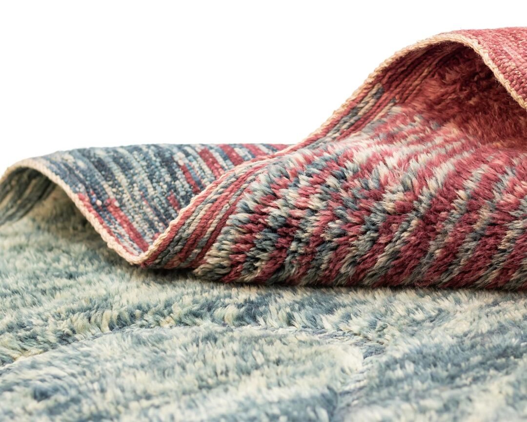 Close-up of a partially folded luxury Moroccan rug featuring intricate textured patterns in red, blue, and gray tones, beautifully displaying both the front and back sides.